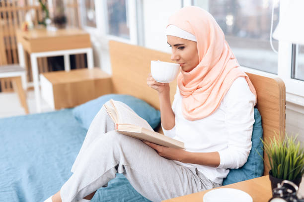 istock An arabian woman is drinking tea and reading a book while sitting on the bed. 1285449647