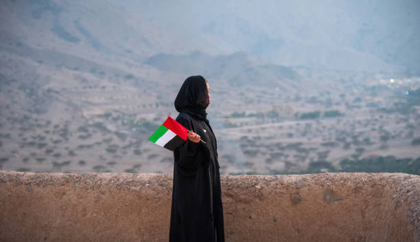 Emirati woman holding UAE flag in the desert mountain at sunset Emirati woman wearing hijab holding United Arab Emirates flag in the desert mountain at sunset jebel hafeet stock pictures, royalty-free photos & images