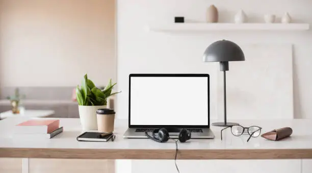 Photo of Place of work. Laptop with blank empty screen, coffee, headset, glasses at home desk