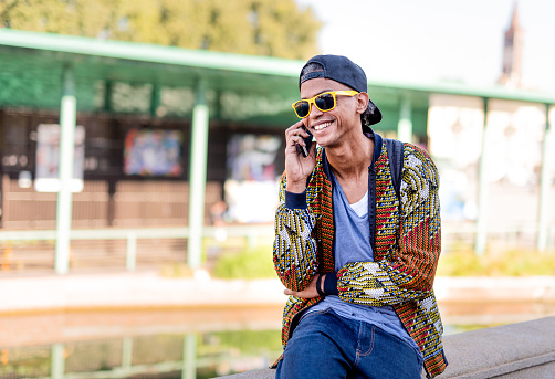 portrait of young stylish black man, trendy young man making a phone call with the mobile, moment of relaxation in urban context of a latin american guy, concept of fashion, diversity and street style