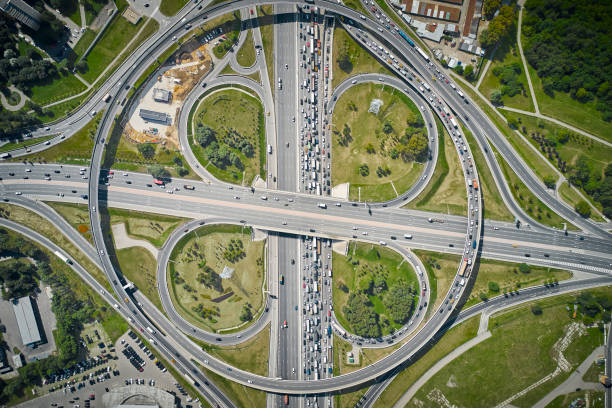 istock Aerial view on the large circular intersection with rounds, curves and clover exits from high altitude. Many cars everywhere. Sunny light. Green plants inside and all around. Camera is looking directly down over the center of crossroad. 1285451231