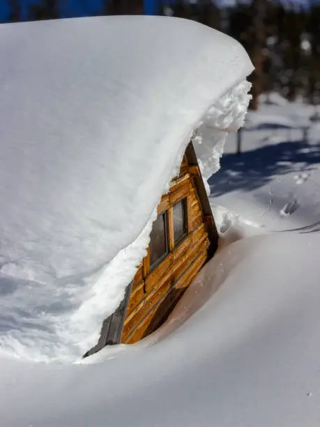 Photo of A wooden house covered with snow. Snowbound hut close-up. Deep white pure snowdrifts in mountains. New Year and Christmas holidays concept.