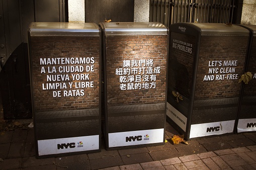 New York, NY, USA - Nov 13, 2020: Three trash cans in a public park with a warning about rats shown in three different languages: Spanish, Chinese and English