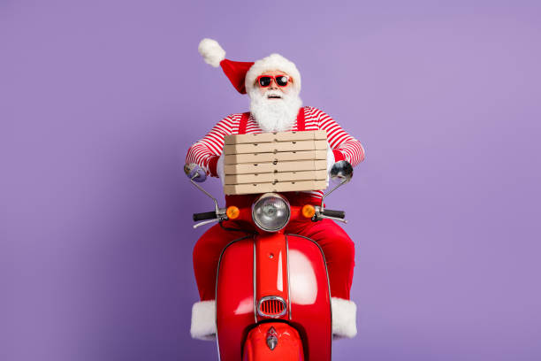 foto di divertente babbo natale giro veloce ciclomotore tenere scatole di pizza indossare x-mas costume a righe camicia berretto occhiali isolati sfondo di colore viola - personal accessory cap christmas santa claus foto e immagini stock