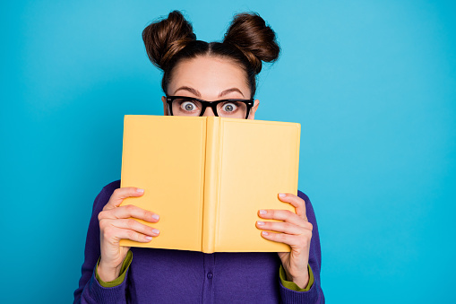 Close-up portrait of her she nice attractive smart clever funny shy schoolgirl hiding behind diary book home task isolated on bright, vivid shine vibrant blue green teal turquoise color background
