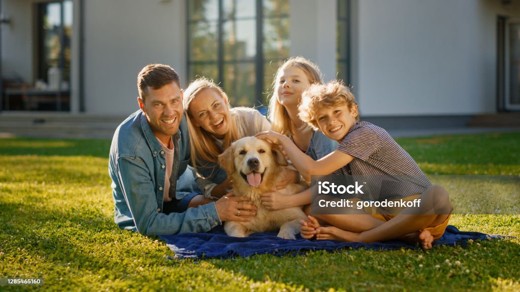 幸せなゴールデンレトリバー犬とポーズをとって、芝生の上でピクニックをしている父、母と息子の肖像画。牧歌的な家族は、夏の家の裏庭で忠実な血統犬の屋外で楽しんでいます。 - 家族のロイヤリティフリーストックフォト