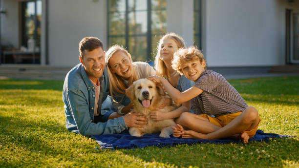 幸せなゴールデンレトリバー犬とポーズをとって、芝生の上でピクニックをしている父、母と息子の肖像画。牧歌的な家族は、夏の家の裏庭で忠実な血統犬の屋外で楽しんでいます。 - golden retriever retriever dog smiling ストックフォトと画像