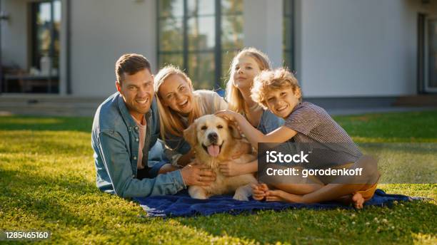 幸せなゴールデンレトリバー犬とポーズをとって芝生の上でピクニックをしている父母と息子の肖像画牧歌的な家族は夏の家の裏庭で忠実な血統犬の屋外で楽しんでいます - 家族のストックフォトや画像を多数ご用意