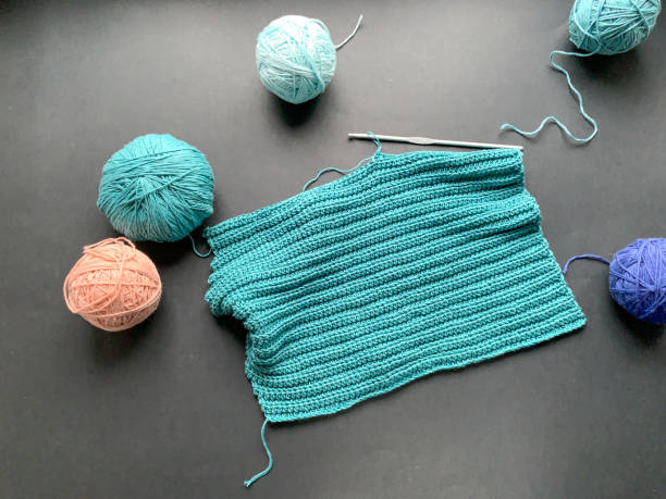 Crocheting process, turquoise thread on a black background. A skein of yarn and a crochet hook. The concept of creating a product with your own hands. Needlework, Hobbies.