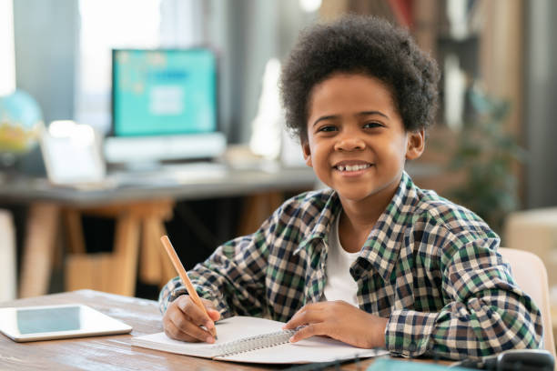 istock Adorable schoolboy making notes in copybook and looking at you with smile 1285467065