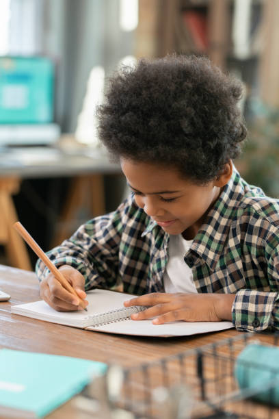 istock Cute elementary schoolboy of African ethnicity making notes in copybook 1285467102