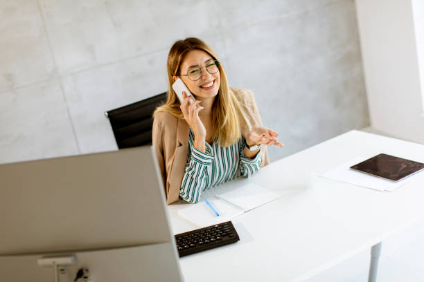 istock Young woman using mobile phone while sitting by the desk in the office 1285468229