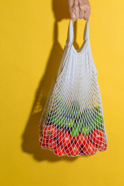istock Male hand holding a white mesh bag with vegetables on yellow background 1285469881