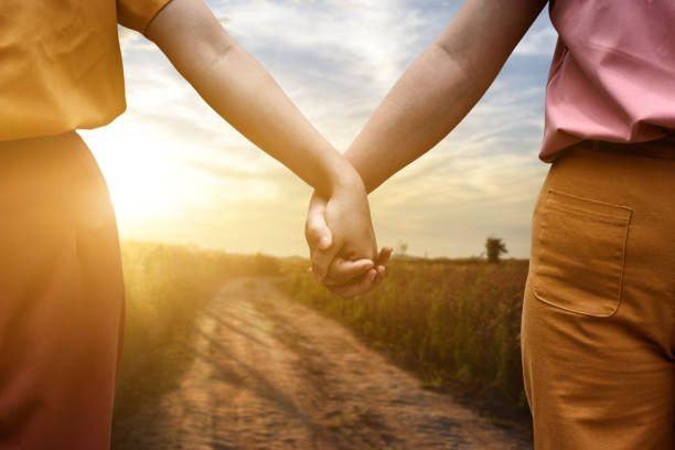 istock Two female holding hands walking on the road at sunset background. 1285469889