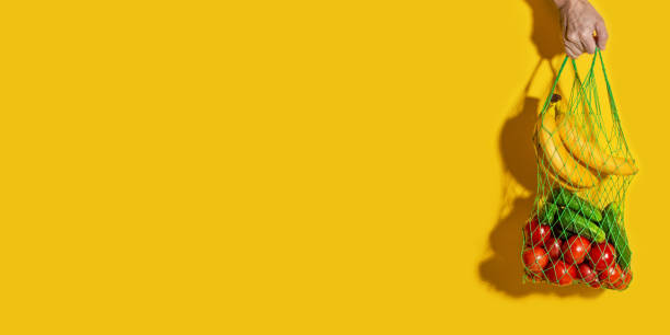 istock Male hand holding a white mesh bag with vegetables on yellow background, banner 1285469934