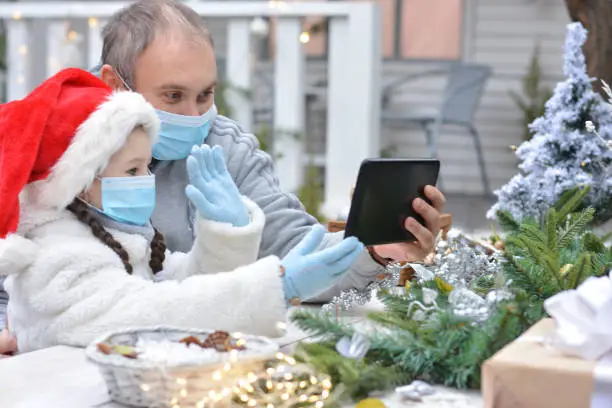 Dad and daughter in protective medical masks and a Santa hat wish Merry Christmas via messenger. Safe happy new year's and Merry christmasgreetings via messenger during quarantine covid 19 concept