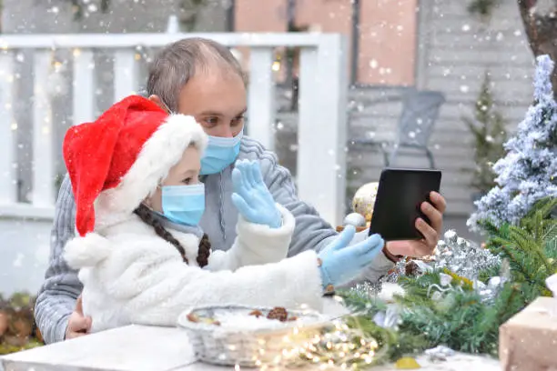 Dad and daughter in protective medical masks and a Santa hat wish Merry Christmas via messenger. Safe happy new year's and Merry christmasgreetings via messenger during quarantine covid 19 concept