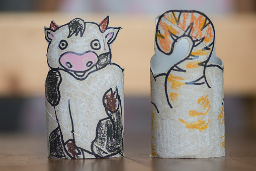 Child hands presenting a DIY activity: Homemade Animal bracelets for kids, made of used toilet paper rolls, featuring Cartoon characters of a cat and a cow.