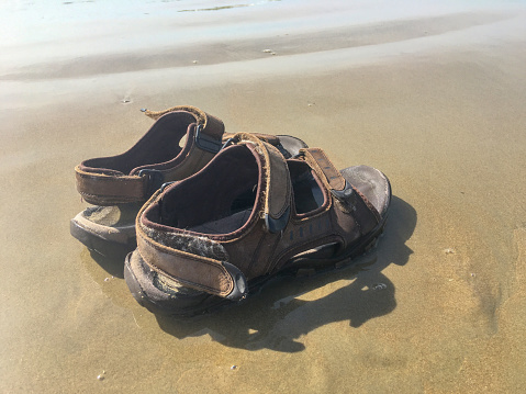 Grunge mens sandals left on wet sand by the sea for summer background