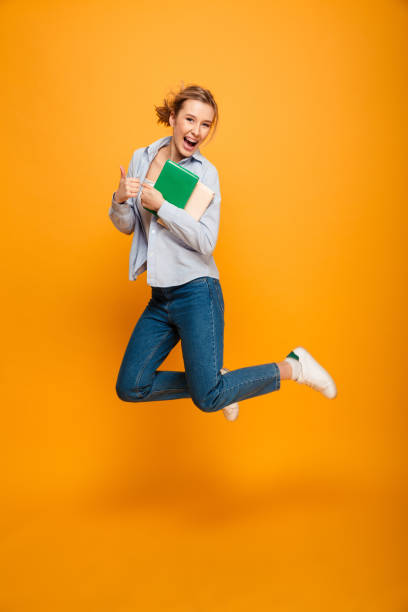 istock Happy young lady student jumping showing thumbs up. 1285473899