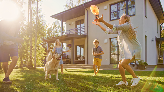 Hermosa familia de cuatro jugar Catch Toy Ball con Happy Golden Retriever Dog en el césped del patio trasero. Idyllic Family tiene diversión con leal pedigrí perro al aire libre en Summer House Backyard. photo