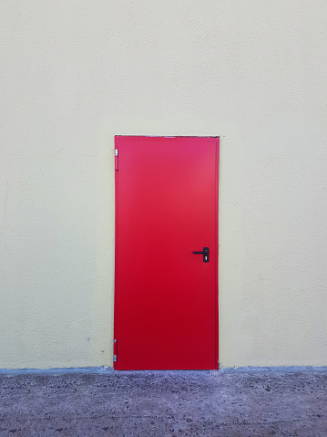 Red Metal door texture with iron handle and concrete wall background.