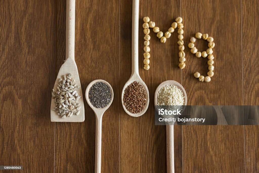Seeds as a source of magnesium Wooden spoons with healthy seeds, and word Mg made of chickpeas arranged on wooden table Magnesium Stock Photo