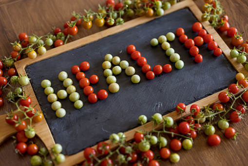 Close up of word health made of red and green cheery tomatoes on black cutting board surrounded by cherry tomato twigs on wooden table
