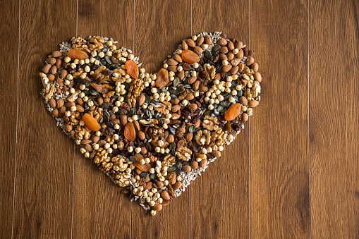 Different mixed nuts and dried fruits forming a heart shape on wooden table