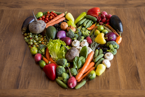 Close up of lot fresh vegetables set in heart shape on wooden table