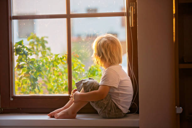 istock Abandoned little toddler boy, sitting sad on a window shield, looking outside at sunset 1285483328