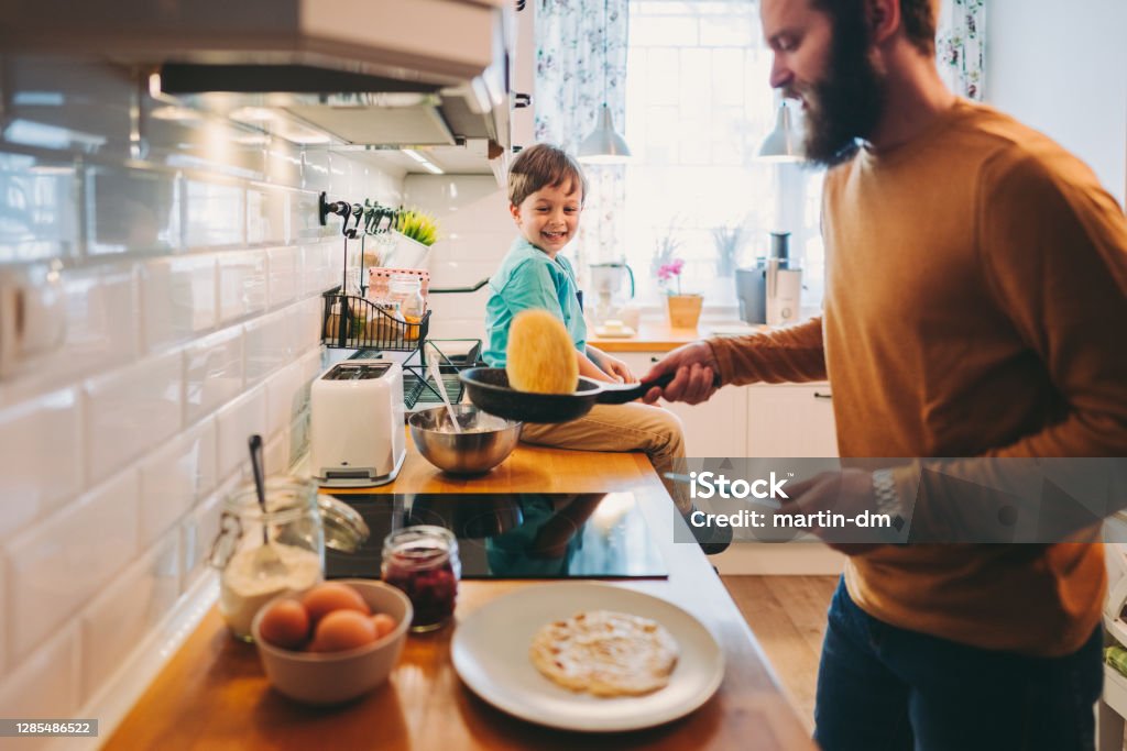 Single father preparing pancakes during COVID-19 lockdown Cute child enjoying to observe his father flipping pancakes in the pan Pancake Stock Photo