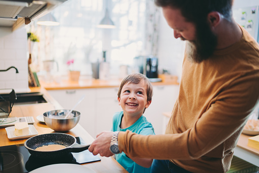 Single father and son preparing pancakes together during the weekend