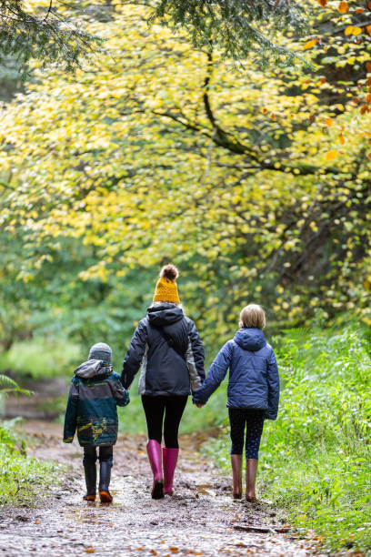 Mother and two children walking away from the camera on a muddy trail. stock photo
