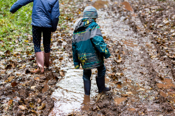 Two children wearing wellies walking through deep mud. stock photo