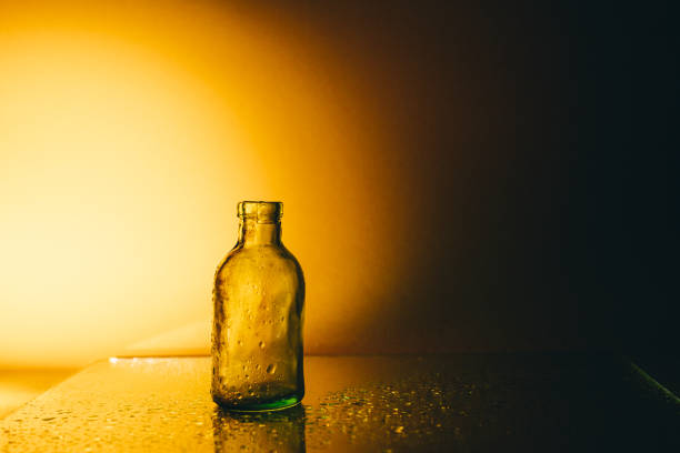 small glass bottle in the shade, lit from the side on a yellow background