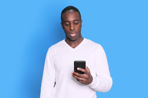 istock Cheerful African American man in white sweater using mobile phone application. 1285493806