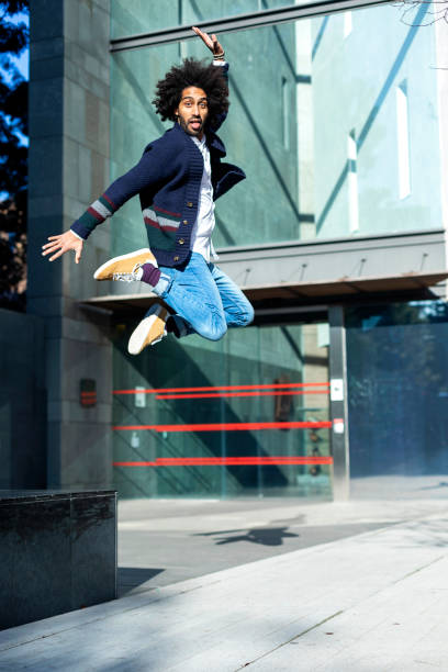 istock Portrait of a young handsome afro black man jumping while looking camera smiling outdoors in a sunny day 1285494582