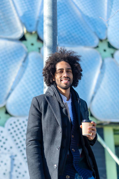 istock Young handsome african american man smiling happy. Standing with smile on face drinking cup of take away coffee at town street. 1285494785