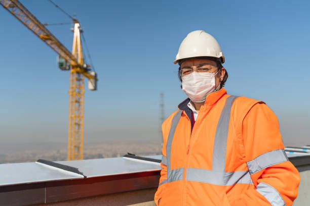 istock Engineer standing in front of the tower crane at the construction site with a hard hat and protective face mask 1285496043