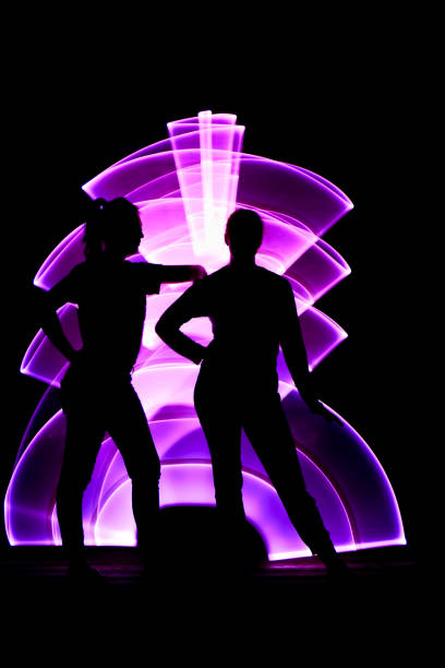 Lightpainting scene with girls. Silhouette of two women in front. Girl leaning on the shoulder of her friend. Abstract curved shape, pink color with a light saber in the background. lightpainting stock pictures, royalty-free photos & images