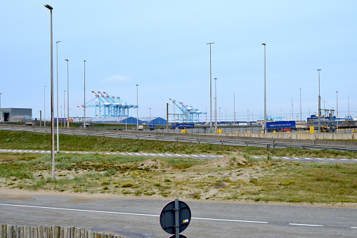 Zeebrugge, West-Flanders, Belgium -  November 11, 2020: Security fence between border Zeebrugge commercial port and Zeebrugge beach. Cranes at the horizon.