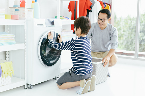Happy smiling Asian family father and son in the laundry load a washing machine. Family activity, Housework, wash and housekeeping concept.