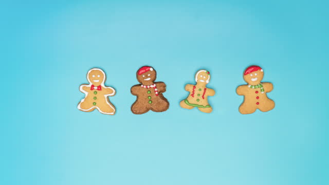 Stop motion flat lay view: making white icing sugar homemade Christmas cookies such as gingerbread with Christmas hat and winter clothes on a table with a blue background. Concept of December holiday in winter and multi-ethnic people.