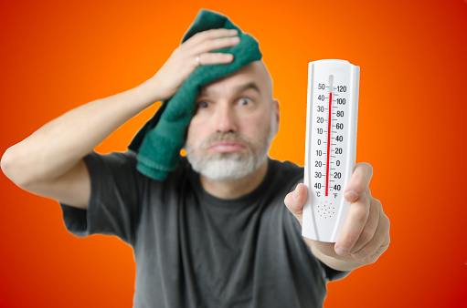 Man holding thermometer during heat wave\nIt shows more than 110F or 40C.\nHe dries his head with a towel