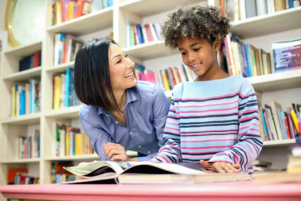 Girl and her teacher in a school library. Two people, about 9-10 years old, mixed multi-ethnic group.