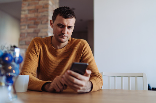 Man sitting at the table and using smartphone at home