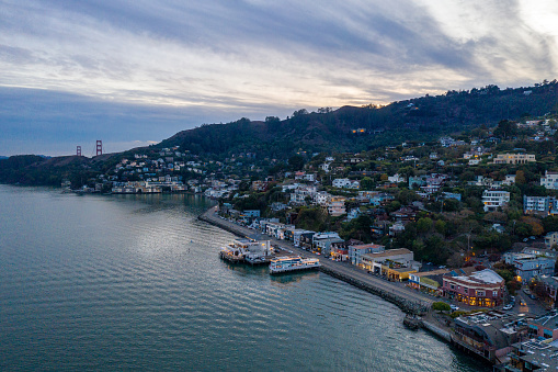 Aerial view of Sausalito at dusk with the Golden gate Bridge looking over the hill. The artistic community is twinkling with lights as the sun sets.