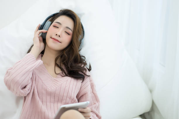 jeune femme asiatique de sourire se détendre et écouter la musique avec des écouteurs. concept d’hiver et de style de vie. - moisturizing cream audio photos et images de collection