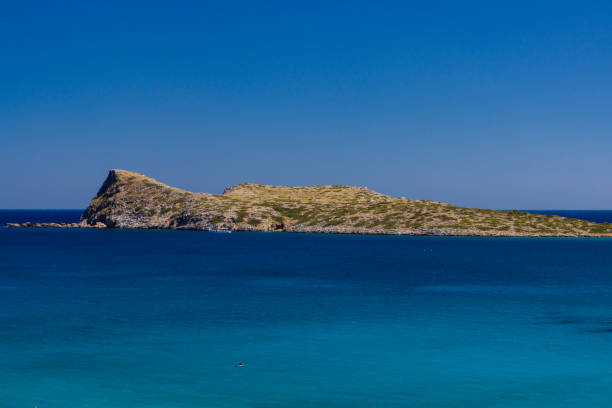 Swimmer in a clear blue ocean near a large, barren island (Kolokitha, Crete, Greece)